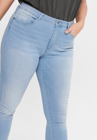 Ανοιχτού μπλε τζιν παντελόνι με ψηλή μέση, στενή γραμμή, πέντε τσέπες, και ξεθωριασμένη υφή, με κλείσιμο μπροστά με κουμπί.