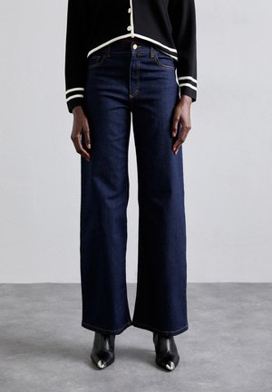 Black buttoned cardigan with white trim, dark blue wide-leg jeans, and black pointed-toe boots with metallic tips on a standing person.