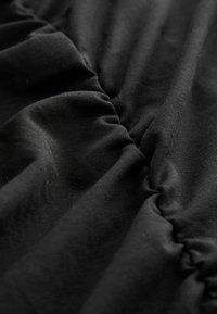 Gros plan sur un tissu noir avec des coutures froncées créant des plis et des rides texturés.