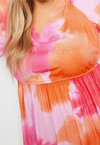 Šaty s výstřihem do V, které mají tie-dye vzor v růžových a oranžových odstínech, s elastickým pasem a splývavou sukní, vyrobené z lehkého materiálu.