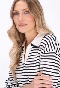 Maglione a maniche lunghe a righe in navy e crema, con colletto e una morbida texture a maglia, con cuciture visibili sul bordo del colletto.