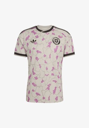 Camiseta de fútbol de color beige claro con racimos de flores rosas, líneas geométricas grises, cuello y ribetes de las mangas en negro, logo de Adidas y escudo de la Federación de Fútbol de Chile.