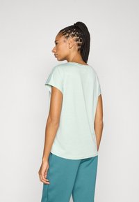 Μπλουζάκι σε απόχρωση μέντας με κοντά μανίκια και άνετη εφαρμογή. Μαλακή υφή και στρογγυλή λαιμόκοψη. Συνδυάζεται με παντελόνι φόρμας σε τιρκουάζ χρώμα.