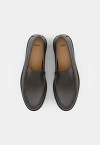 Černé kožené slip-on boty s hladkým povrchem, zaoblenou špičkou a kontrastním prošíváním. Interiér má béžovou stélku s logem.