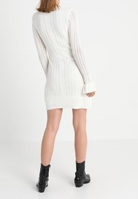 Abito bianco lavorato a maglia con maniche lunghe, strisce verticali texture, orlo a coste e sottomaniche a campana, abbinato a stivali neri alla caviglia.