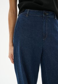 Dunkelblaue Jeanshose mit hoher Taille, mit einem Reißverschluss vorne, Seitentaschen und subtilen Nähdetails.