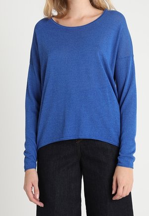 Top blu lungo con maniche a sbuffo realizzato in un tessuto morbido e leggero. Presenta una scollatura rotonda e una vestibilità comoda. Abbinato a pantaloni in denim scuro.