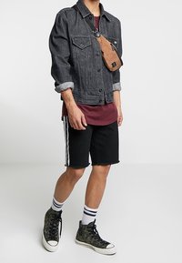 Chaqueta de mezclilla negra, camiseta burdeos, pantalones cortos negros con rayas blancas, zapatillas de lona altas camuflaje y bolso cruzado marrón. Diseño casual.