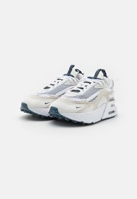 Chaussures de sport blanches et beiges avec panneaux en mesh, col rembourré et accents bleus. Semelle avec coussin d'air notable et semelle extérieure en caoutchouc texturé.