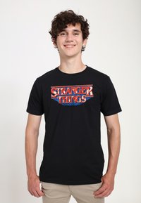 Sort bomuld T-shirt med "Stranger Things"-logo i rød og blå, med korte ærmer og rund hals.