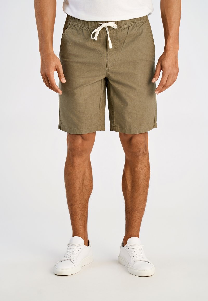 Szorty w kolorze khaki z elastycznym pasem i sznurkiem do wiązania. Posiadają dwie boczne kieszenie i prosty krój. Noszone z białymi sneakersami.