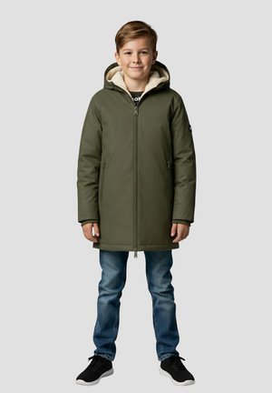 Olijfgroene geïsoleerde parka met een ritssluiting aan de voorkant, dubbele zakken en een beige fleecevoering, gedragen over een blauwe spijkerbroek en zwarte sneakers.