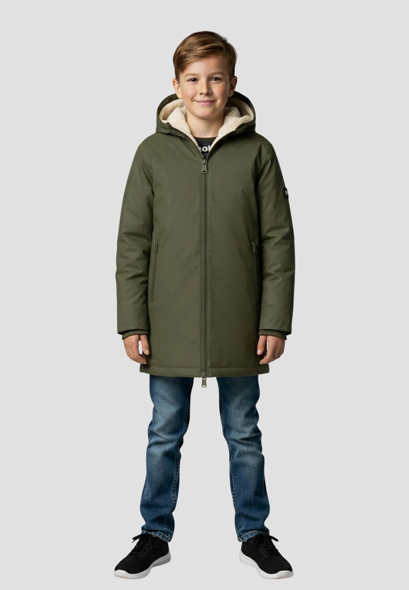 Parka isolante vert olive avec fermeture éclair à l'avant, deux poches, et une doublure en polaire beige, portée sur un jean bleu et des baskets noires.