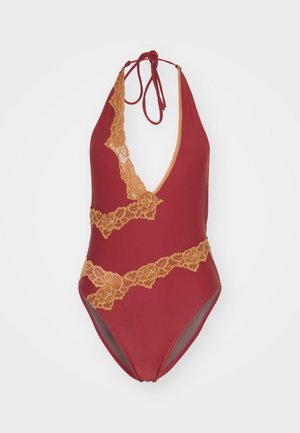 Crvena jednodijelna kupaćica s dubokim V-izrezom, ukrašena zlatnim čipkastim detaljima i vezanjem na leđima. Glatka tkanina s blagim sjajem.