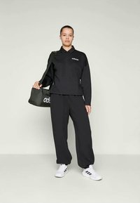 Svart treningsantrekk med langermet polo og matchende bukser. Materialet er glatt, med en logo som detalj på brystet. Brukes med hvite joggesko.