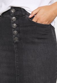 Falda de mezclilla negra con un diseño ajustado, cierre frontal de cinco botones y bolsillo lateral. Textura suave con un desvanecimiento mínimo y sin patrones.