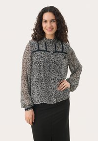 Mörkblå blus med blommönster, genomskinliga långa ärmar, gathered manschetter och en rynkad halsringning. Designen har kontrasterande marinblå detaljer och knappar.