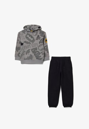 Sudadera con capucha gris con gráficos de Batman y pantalones de chándal negros. La sudadera tiene un bolsillo frontal; los pantalones tienen una cintura elástica.