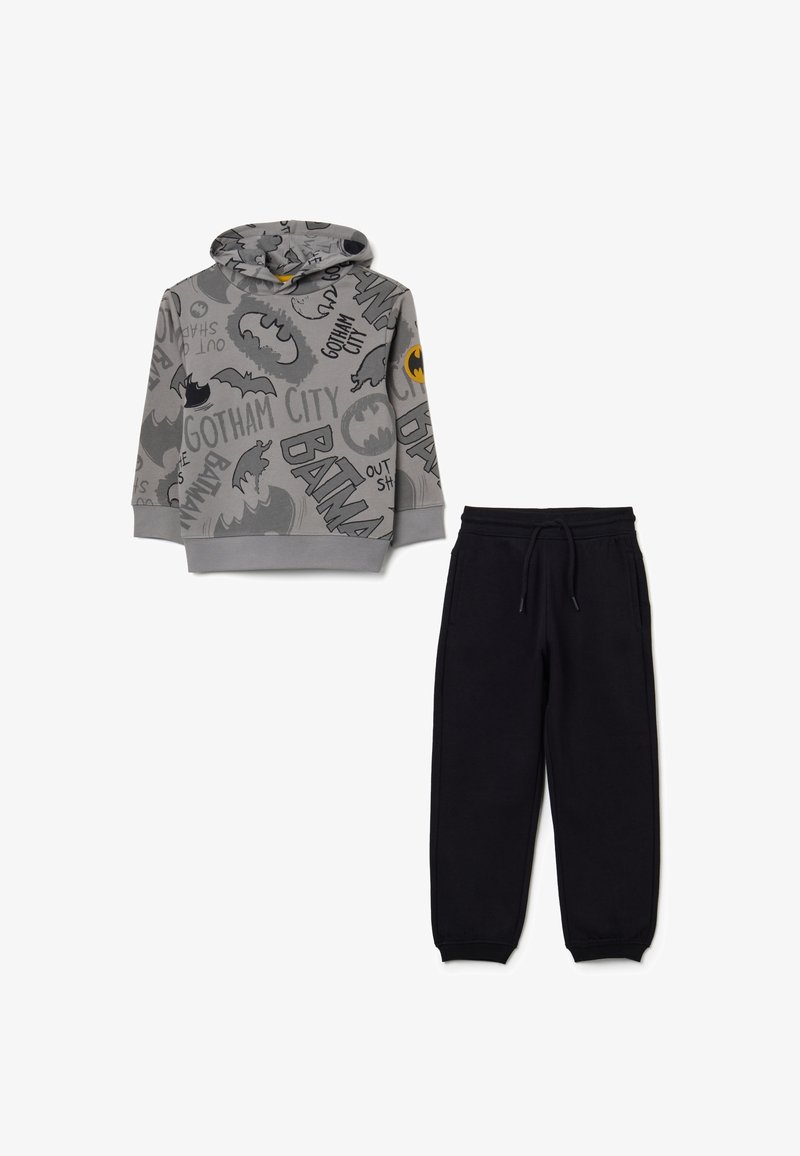 Felpa grigia con cappuccio e grafiche di Batman, abbinata a pantaloni della tuta neri. La felpa presenta una tasca frontale; i pantaloni hanno un elastico in vita.