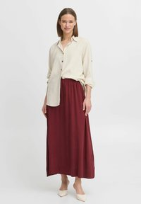 Fustă lungă burgundă asortată cu o cămașă bej deschis, cu nasturi, având mâneci răsucite și o croială lejeră. Finisaj textil neted.