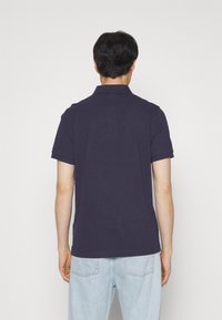 T-shirt polo bleu marine avec un col classique et des manches courtes, fabriquée en tissu doux. Associé à un jean en denim bleu clair.
