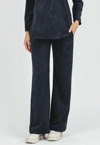 Pantaloni in velluto a coste di colore blu navy, con taglio a gamba larga, morbido al tatto e vestibilità casual, abbinati a scarpe chiare con suola spessa.