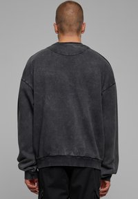 Felpa nera oversize con una texture leggermente consumata, polsini e orlo a costine e scollo rotondo. Vista posteriore, senza motivi o grafiche.