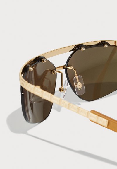 Gold-tone sunglasses with dark brown lenses, featuring a thin, curved frame, adjustable nose pads, and textured temples.
