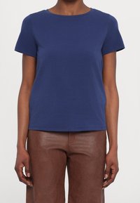 Camiseta de algodón azul marino con cuello redondo y mangas cortas. Textura suave, corte relajado y dobladillo recto. Combinada con pantalones de cuero marrón.