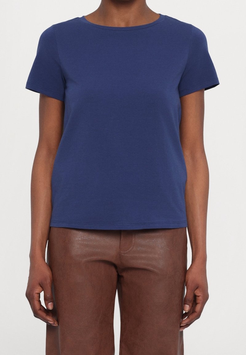 Camiseta de algodón azul marino con cuello redondo y mangas cortas. Textura suave, corte relajado y dobladillo recto. Combinada con pantalones de cuero marrón.