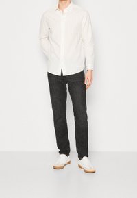 Chemise à manches longues à rayures blanches avec boutons, associée à un jean foncé et des baskets blanches à semelle gomme. Design et coupe simples et contemporains.