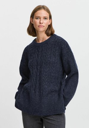 Navy blue knitted sweater with a cable pattern, round neckline, and long sleeves. Paired with dark gray pants, set against a plain background.