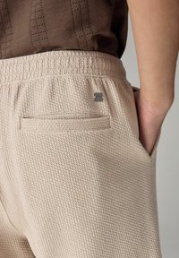 Beige strukturerede shorts med et vævet mønster, elastisk talje og en baglomme, der har en lille metallogo-detalje.