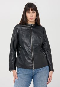 Giacca in pelle nera con colletto alto, chiusura a zip, tasche laterali e design aderente. La superficie è liscia e le cuciture sono ben rifinite.