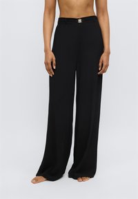 Platas melnas bikšu ar platiem galiem un gludu tekstūru, ar šauru jostasvietu un metālisku sprādzes detaļu priekšpusē.