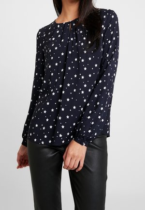 Blusa blu navy con motivo a stelle bianche, con fronte plissettata, scollo rotondo e maniche lunghe arricciate, abbinata a pantaloni neri simili alla pelle.