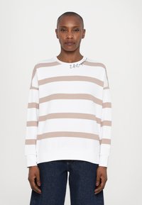 Hvit hettegenser med beige horisontale striper, rund hals og lange ermer. Teksten "EASE" trykt på kragen. Kombinert med mørk denim.
