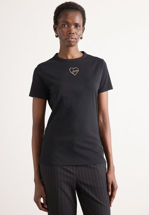 Zwarte katoenen t-shirt met korte mouwen, voorzien van een goud geborduurd hart en handtekening op de borst. Eenvoudig, aansluitend ontwerp.