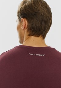 Burgundowa koszulka z krótkim rękawem o gładkiej fakturze, z białym logo nadrukowanym na tylnym karku.