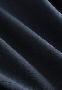 Ciemnoniebieska tkanina o teksturowanej powierzchni z widocznym splotem, charakteryzująca się miękkimi fałdami i subtelnym blaskiem. Idealna do odzieży lub zastosowań tapicerskich.