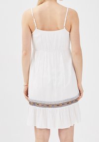Weißes ärmelloses Kleid mit elastischem Bund, ausgestelltem Saum und mehrfarbigen bestickten Akzenten am unteren Rand, gefertigt aus leichtem Stoff.