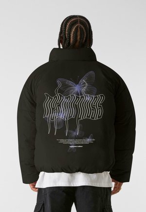 Schwarze Daunenjacke mit einem großen lila Schmetterlingsgrafik und stilisiertem Text auf dem Rücken. Das Material wirkt glatt und gepolstert.