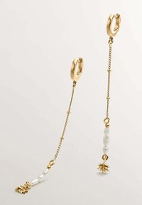 Pendientes de aro dorados con cadenas colgantes, que presentan perlas blancas y charms de piña. Texturas suaves con acentos brillantes, diseño ligero.