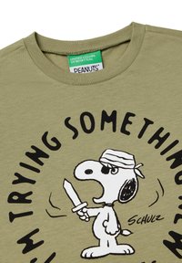 Olivenfarbener T-Shirt mit einem Cartoon-Hund, der ein Schwert hält, umgeben von dem Text "ICH PROBIERE ETWAS" in fettem Schwarz.