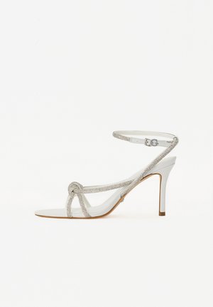 Valge kõrge kontsaga sandaal tekstuurse rihmaga, mis sisaldab sädelusi, avatud varba disain ja sääre rihm reguleeritava pandlaga.
