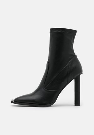 Sort ankelstøvle lavet af glat læder, med spids tå, høj stilettohælh og elastiske sidestykker for nem påtagning.