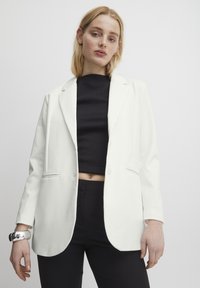 Bílý blazer s jedním knoflíkem, klopami, postranními kapsami a hladkou texturou, nošený přes černý crop top.