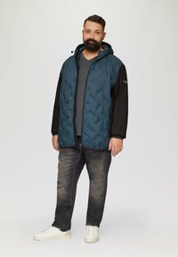 Padded jacket z górną częścią w odcieniu turkusowym i czarnymi rękawami, z kapturem, zamek błyskawiczny z przodu oraz teksturowanym wzorem. Nosi się na szarym T-shircie.