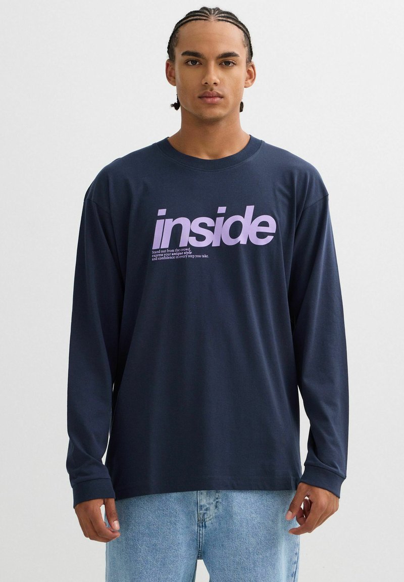 Camiseta de manga larga en color azul marino con un gran gráfico morado de "inside" y texto debajo. Fabricada en tejido suave con un corte holgado y escote redondo.