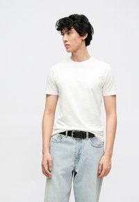 Wit T-shirt met korte mouwen en een ronde hals, gecombineerd met lichtblauwe loszittende jeans en een zwarte riem met een zilverkleurige gesp.